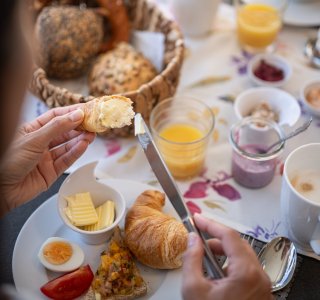 Am Tisch wird ein leckeres Frühstück mit Croissants, Eiern und Marmelade vorbereitet. Gemütliche Atmosphäre im Garten.