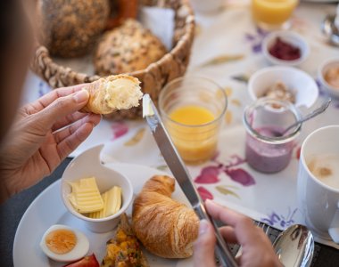 Am Tisch wird ein leckeres Frühstück mit Croissants, Eiern und Marmelade vorbereitet. Gemütliche Atmosphäre im Garten.