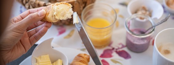 Am Tisch wird ein leckeres Frühstück mit Croissants, Eiern und Marmelade vorbereitet. Gemütliche Atmosphäre im Garten.