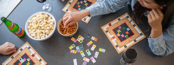 Eine Familie spielt Brettspiele. Auf dem Tisch stehen Snacks und Getränke, während sie lachen und Spaß haben.
