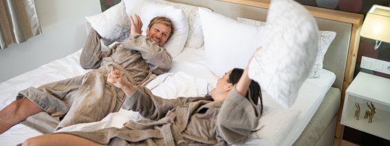 Ein Paar hat Spaß im Hotelzimmer und wirft Kissen im Bett. Es ist eine entspannte Zeit in einem modernen Raum.