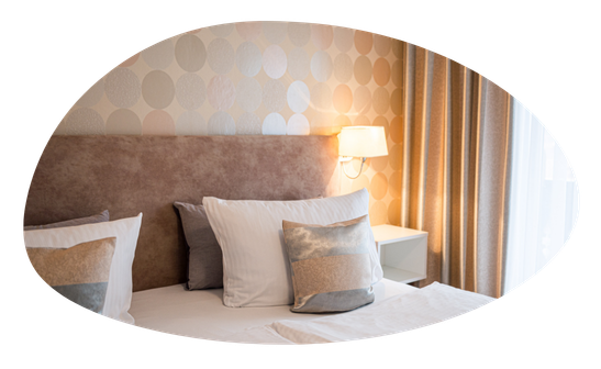 Ein Schlafzimmer mit einem großen Bett und einem Fenster. Es gibt Kissen auf dem Bett und eine Lampe auf dem Tisch.