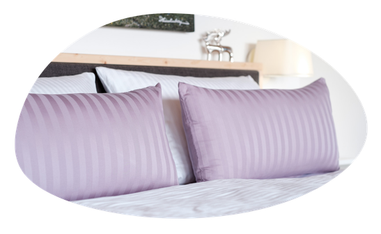 Zwei Kissen liegen auf einem Bett in einem Schlafzimmer. Eine Lampe steht auf einem Nachttisch.