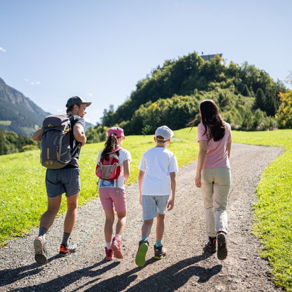Eine Familie wandert auf einem Weg durch die Berge unter blauem Himmel. Die beiden Kinder sind mit ihren Eltern unterwegs.