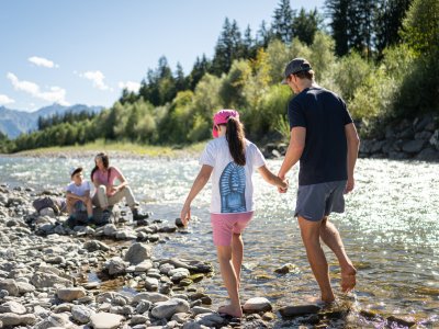 Eine Familie spielt am Flussufer. Sie gehen über Steine und genießen die Natur.