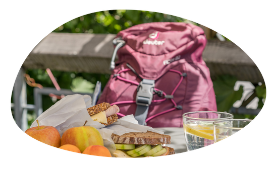 Auf einer Terrasse liegt ein Rucksack. Daneben gibt es Essen mit Obst und zwei Gläser Wasser.