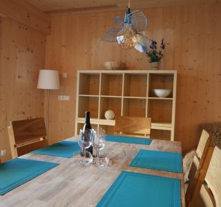 Ein stilvolles Esszimmer mit einer großen Holztafel und blauen Tischsets. Die Einrichtung ist hell und einladend.