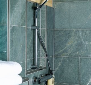 In einem modernen Badezimmer ist eine Dusche mit grauen Fliesen und einem stylischen Duschkopf installiert.