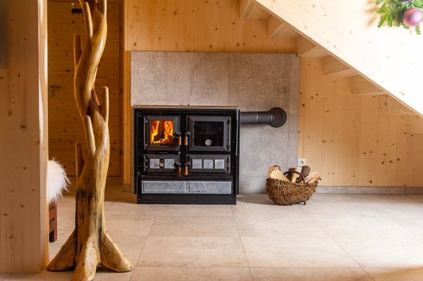 Holzofen sorgt für Wärme in einem gemütlichen Raum Ein Holzofen brennt in einem hellen Raum mit Holzregalen. Der Raum strahlt Gemütlichkeit und Wärme aus.