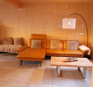 In einem warmen Holzraum steht ein bequemes, oranges Sofa neben einem rustikalen Holztisch.