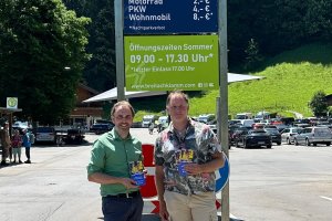 Regionenlotse Joachim Weiler von fahrmob.eco und Dominik Fritz, Betriebsleiter der Breitachklamm stehen mit Fahrmob-Flyern in der Hand vor dem Parkplatz der Breitachklamm.