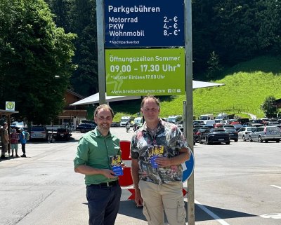 Regionenlotse Joachim Weiler von fahrmob.eco und Dominik Fritz, Betriebsleiter der Breitachklamm stehen mit Fahrmob-Flyern in der Hand vor dem Parkplatz der Breitachklamm.