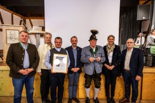 Sechs Personen stehen auf der Bühne, sie halten eine Auszeichnung und einen Pokal in der Hand. Es ist Abend und eine Feier.