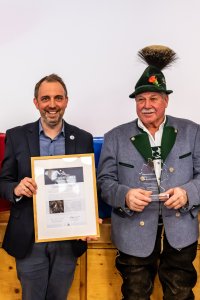 Vier Personen stehen auf einer Bühne und präsentieren eine Urkunde. Es ist eine feierliche Veranstaltung in einem Saal.