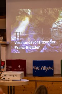 Grußwort in einem Saal. Zuschauer hören ihm zu und sind aufmerksam.