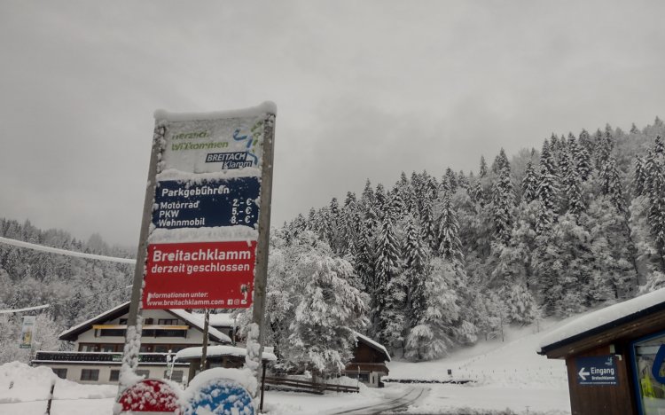 Ein Parkplatz an einer Sehenswürdigkeit bei Schnee. Ein Schild zeigt die Gebühren und den Geschlossen-Status der Breitachklamm.