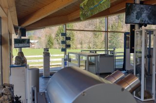 Das Besucherzentrum zeigt Informationsstände und Geräte zur Erklärung der Umgebung. Draussen sind Bäume und Landschaft sichtbar.