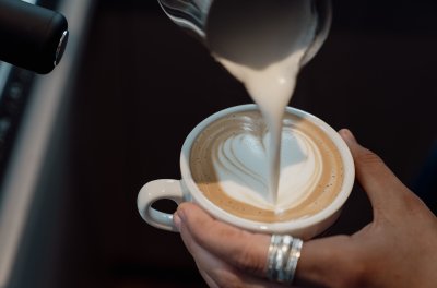 Eine Person gießt heiße Milch in einen Kaffee und formt ein Herz auf der Oberfläche. Der Moment zeigt Handarbeit in einem Café.