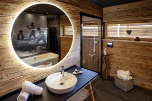 Badezimmer im Chalet Holzar, mit eigener Sauna, Badewanne und Regendusche, die Türe führt zur privaten Sauna im Chalet.