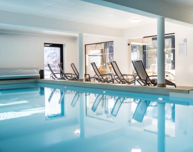 Im Wellnessbereich stehen Liegen neben einem ruhigen Schwimmbad. Das Licht kommt durch große Fenster.