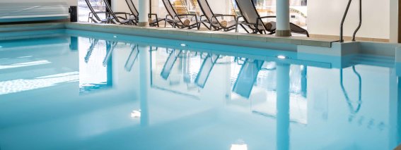 Im Wellnessbereich stehen Liegen neben einem ruhigen Schwimmbad. Das Licht kommt durch große Fenster.