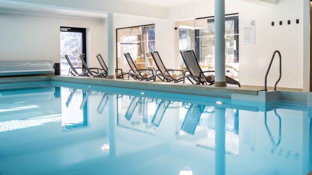 Im Wellnessbereich stehen Liegen neben einem ruhigen Schwimmbad. Das Licht kommt durch große Fenster.