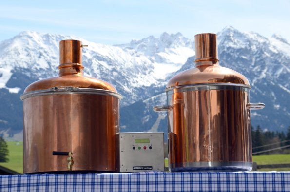 Kupferne Brennblasen stehen vor einer beeindruckenden Bergkulisse in den Alpen und warten auf die Destillation.