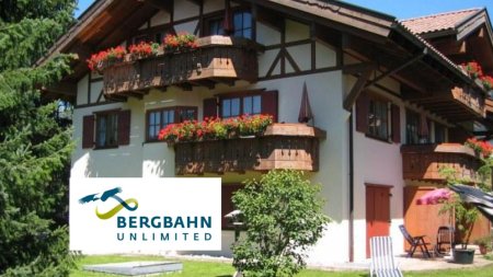 Ein traditionelles Haus steht in einer schönen Umgebung. Blumen schmücken die Balkone und es gibt Gartenmöbel.