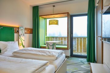 Neben einem gemütlichen Doppelbett und findest Du im Panoramafenster eine tolle Sitzgelegenheit um die Füße hochzulegen und den Blick auf die oberbayrischen Berge aus dem Explorer Hotel Garmisch zu genießen.