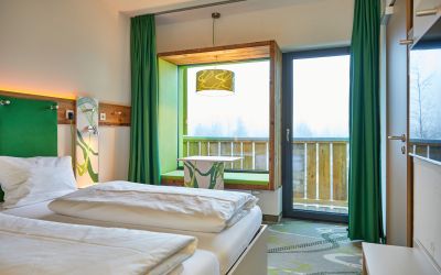Neben einem gemütlichen Doppelbett und findest Du im Panoramafenster eine tolle Sitzgelegenheit um die Füße hochzulegen und den Blick auf die oberbayrischen Berge aus dem Explorer Hotel Garmisch zu genießen.