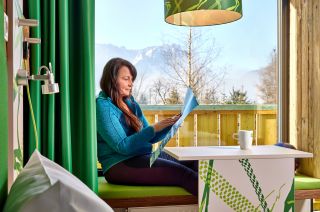 Das Explorer Hotel Zimmer in Farchant, ist im frischen grün gehalten und bietet Dir eine gemütliche Sitzbank im Panoramafenster.
