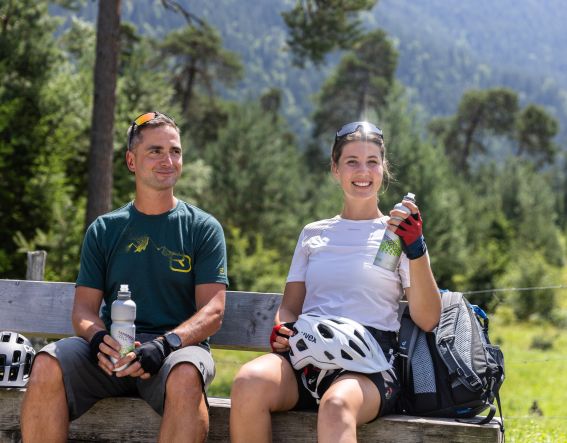 Bei einer Mountainbiketour in den Alpen kannst Du bei einer Trinkpause die Aussicht auf die Berge genießen. Bevor es mit dem MTB weitergeht.