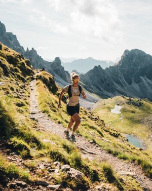 Eine Trailrunnerin rennt einen schmalen Bergpfad entlang, im Hintergrund sind die Berge der Stubaier Alpen zu sehen.