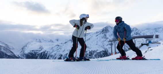 Two skiers stand laughing on the piste in front of a mountain backdrop at the Gaislachkogel. Best mood on snow: Two skiers enjoy the slopes and the panorama together at the Gaislachkogel in the Ötztal valley.