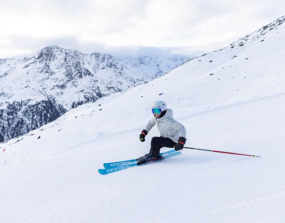 Skifahrerin carvt auf der Piste am Gaislachkogel vor verschneiter Ötztaler Bergkulisse. Dynamische Schwünge vor großer Kulisse: Vom Explorer Hotel Ötztal aus bist Du schnell mitten im Skigebiet Gaislachkogel unterwegs.