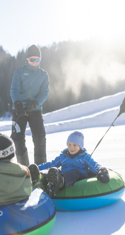 Familie zieht Snowtubes auf einer sonnigen Winterbahn im Ötztal – gemeinsames Schneeabenteuer mit Kindern in Tirol