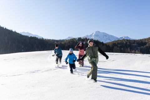 Rodina se smíchem běží přes slunnou zasněženou oblast v údolí Ötztal s výhledem na tyrolské hory.