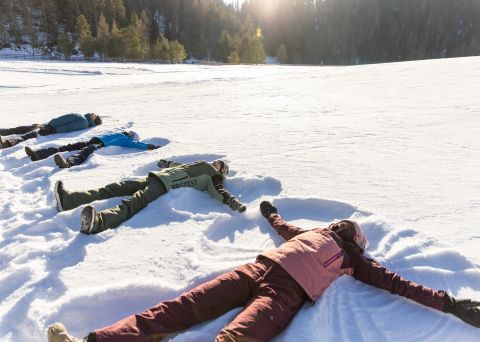 Una famiglia si rilassa nella neve, creando angeli di neve in un soleggiato prato invernale nella valle dell'Ötztal.