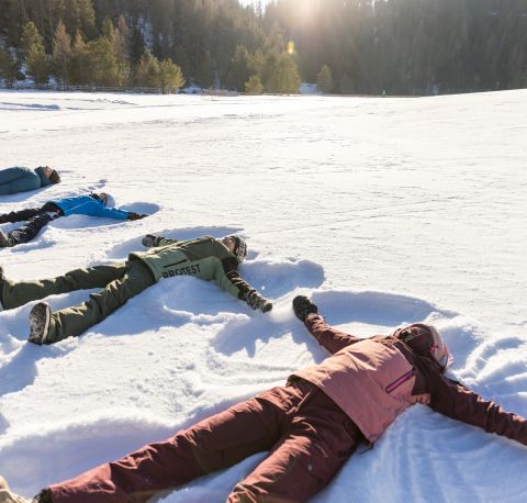 Een gezin ligt in de sneeuw en maakt sneeuwengelen op een zonnige winterweide in het Ötztal.