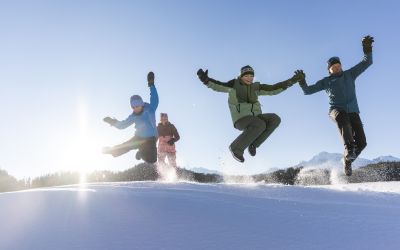 Familie springt gemeinsam über eine Schneekuppe im Ötztal – energiegeladene Winteraction mit Kindern in Tirol
