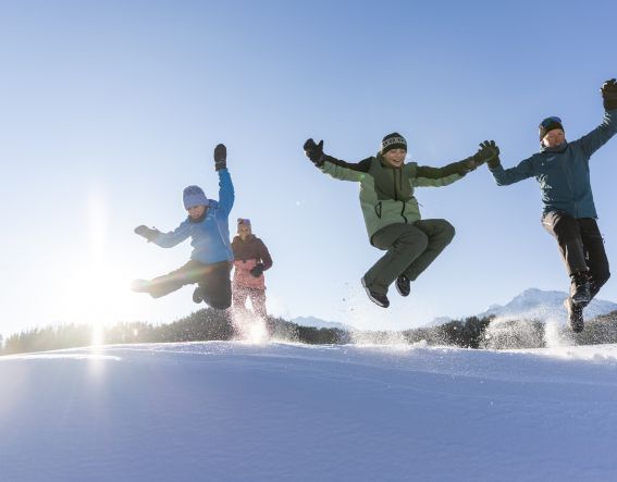 Familie springt gemeinsam über eine Schneekuppe im Ötztal – energiegeladene Winteraction mit Kindern in Tirol