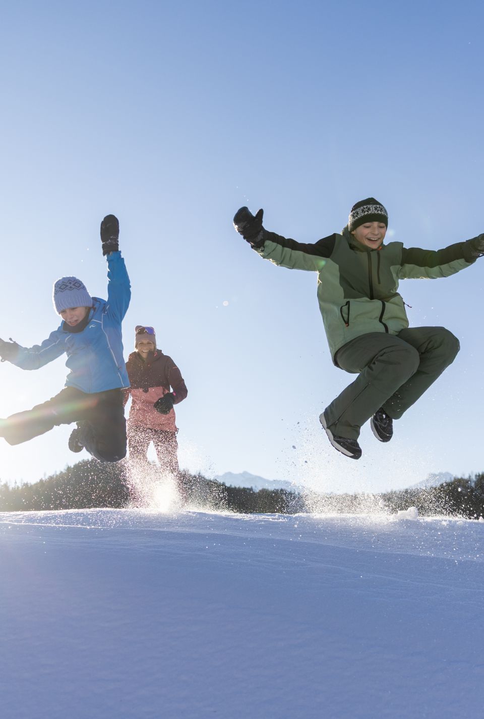 Familie springt gemeinsam über eine Schneekuppe im Ötztal – energiegeladene Winteraction mit Kindern in Tirol