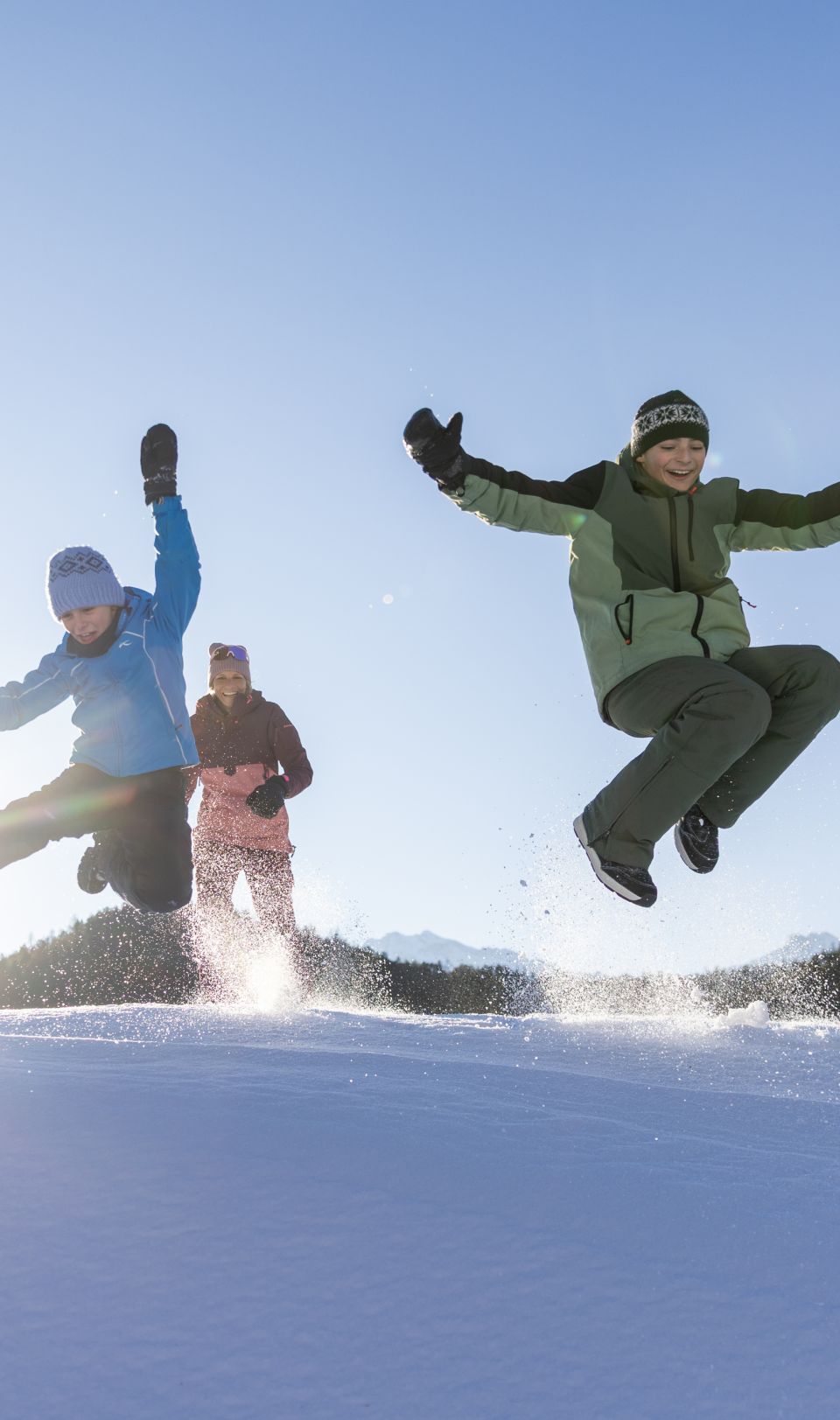 Une famille saute ensemble par-dessus une congère dans la vallée de l'Ötztal – une activité hivernale pleine d'énergie avec des enfants au Tyrol