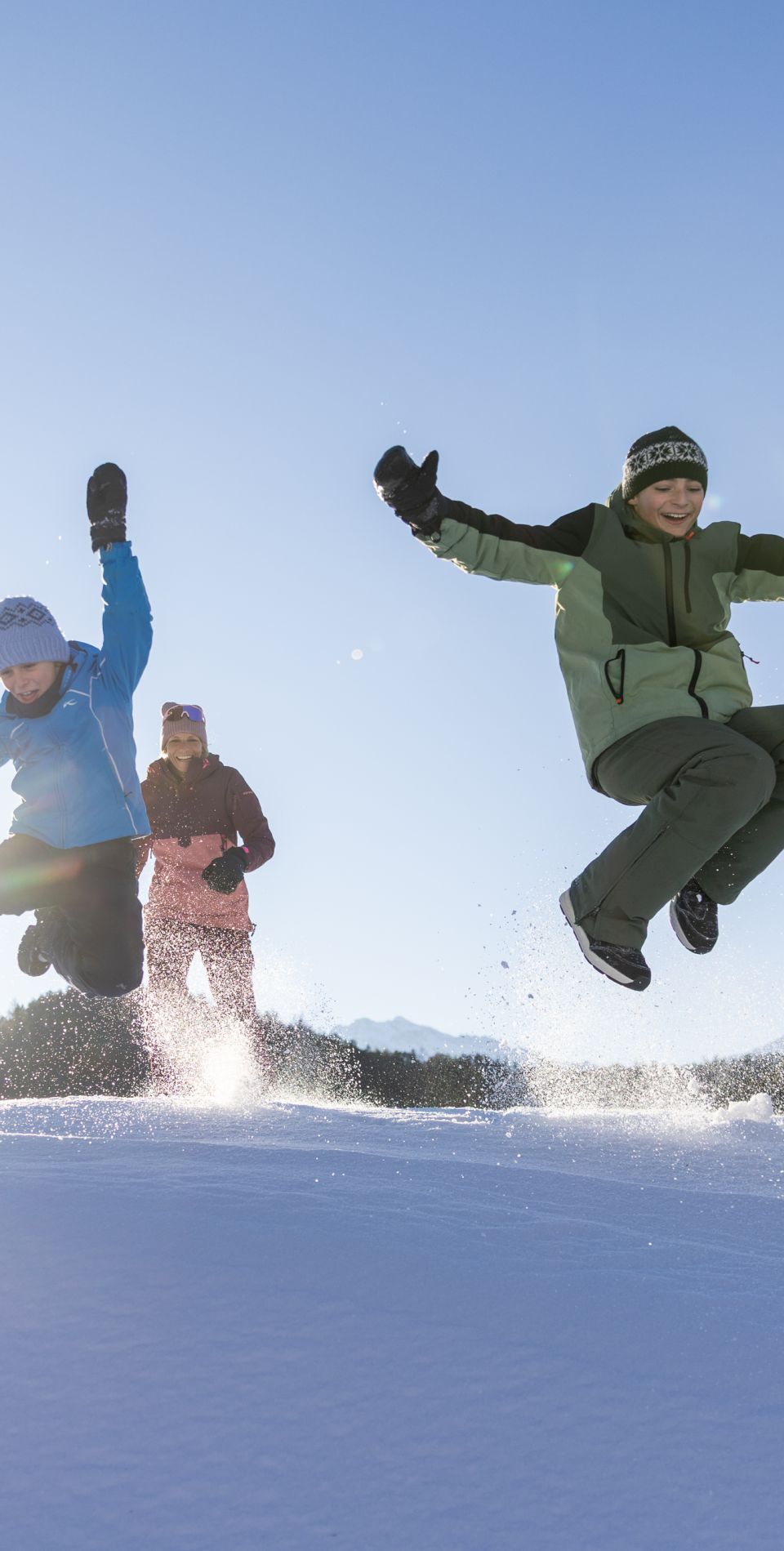 Una famiglia salta insieme sopra un cumulo di neve nella valle dell'Ötztal: un'avventura invernale ricca di energia con i bambini in Tirolo.