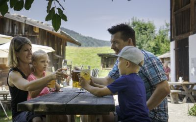 A family sits on a bench in the shade and enjoys a cool drink.