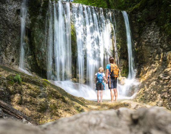 Mutter und Tochter schauen sich einen Wasserfall an. Ein Pärchen schaut sich einen Wasserfall an.