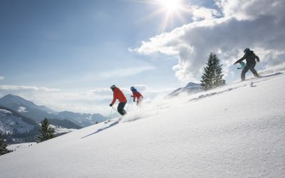 Mehrere Skifahrer genießen den strahlenden Sonnenschein beim hinunterfahren ins Tal.