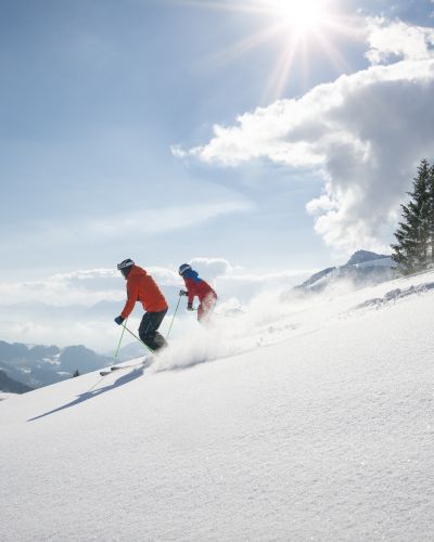 Mehrere Skifahrer genießen den strahlenden Sonnenschein beim hinunterfahren ins Tal.