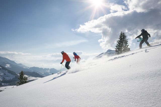 Mehrere Skifahrer genießen den strahlenden Sonnenschein beim hinunterfahren ins Tal.