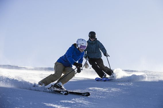 Due persone stanno sciando giù per il monte Sudelfeld sotto il sole.